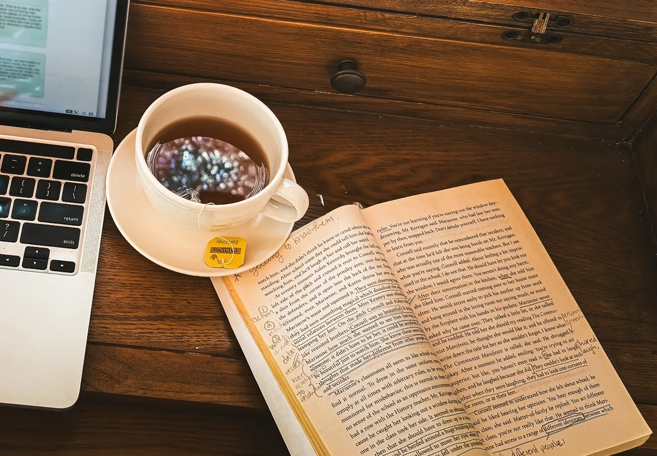 A cup of tea beside an open, annotated paperback on the writing desk